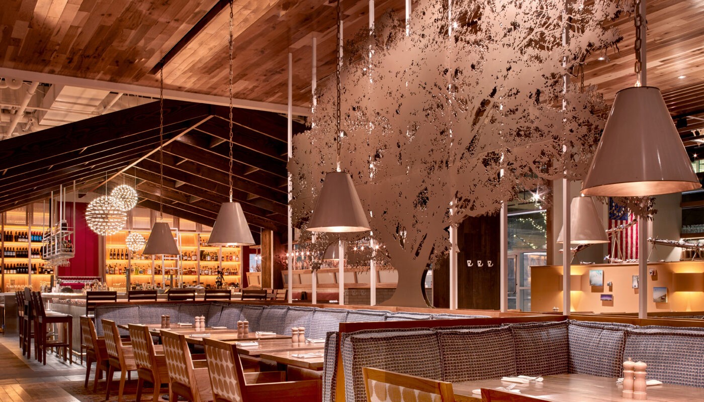 Inviting interior at Founding Farmers Tysons featuring wood-paneled ceilings, a decorative metal tree centerpiece, and booth seating with pendant lighting.