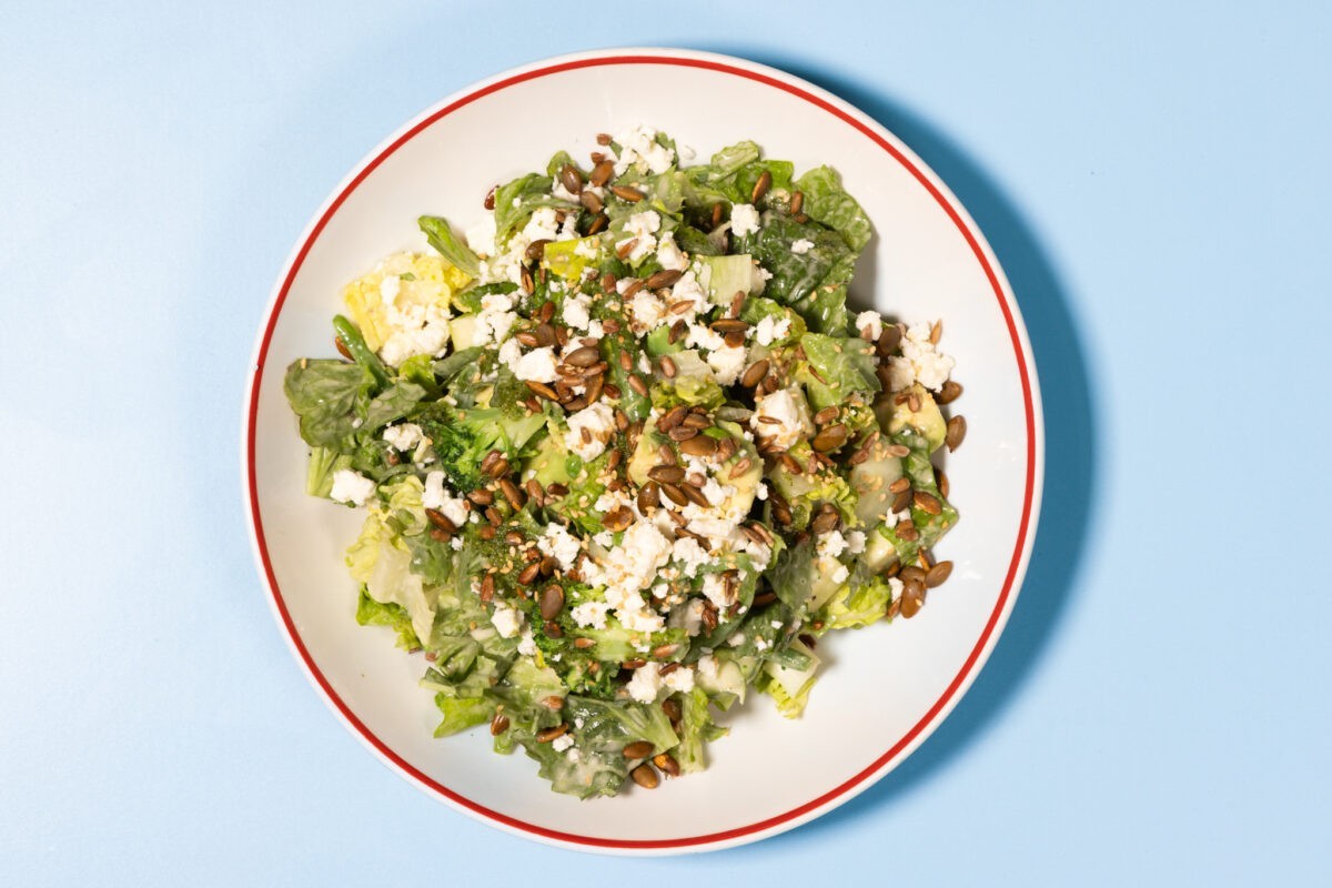 Good All Green Salad topped with green beans, broccoli, green apple, avocado, feta cheese, and toasted seeds on a bed of mixed greens.
