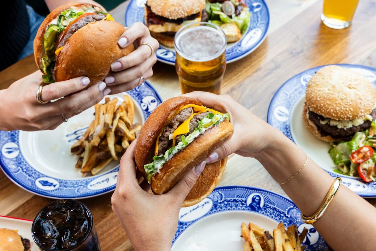 Close-up of juicy cheeseburgers being held at the table at Founding Farmers—one of DC’s top spots for the best burgers. Served with hand-cut fries, cold drinks, and vibrant salads on signature blue-and-white plates.