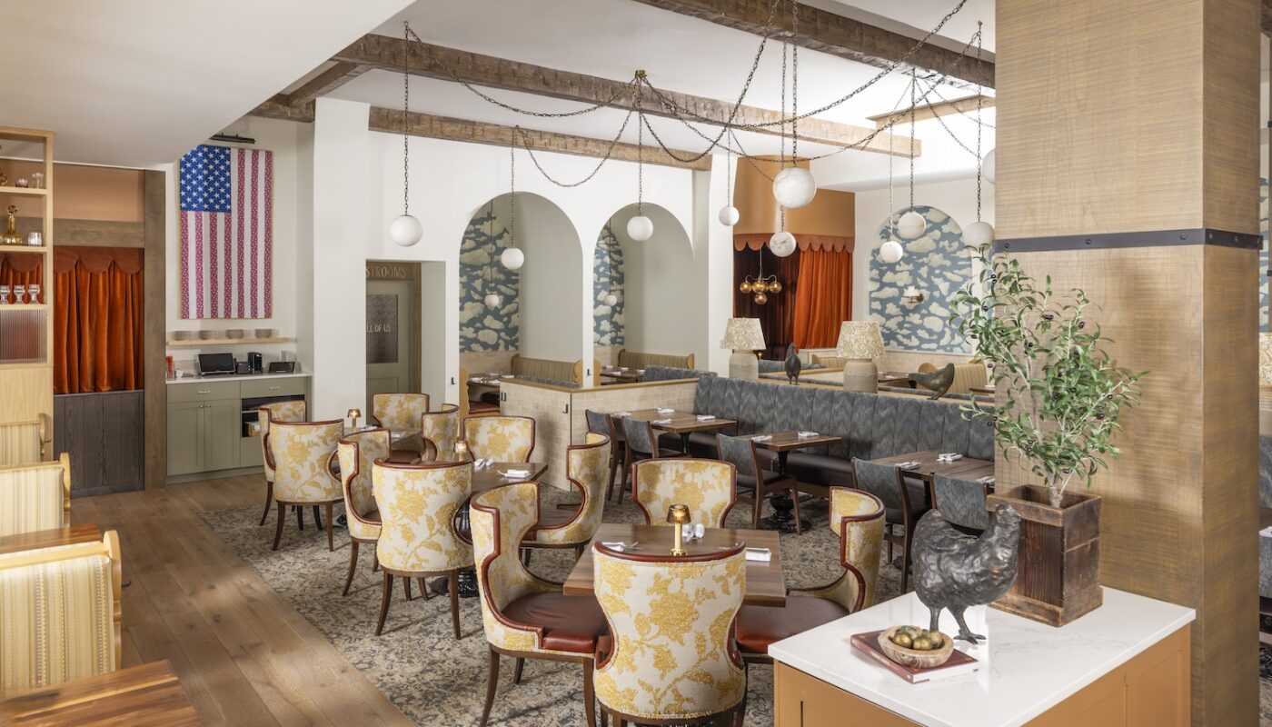 Spacious dining room at Founding Farmers Alexandria with floral yellow armchairs, cloud mural arches, cozy booths, globe pendant lights, and Americana decor including a red, white, and blue flag artwork.