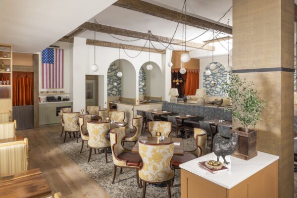 Spacious dining room at Founding Farmers Alexandria with floral yellow armchairs, cloud mural arches, cozy booths, globe pendant lights, and Americana decor including a red, white, and blue flag artwork.