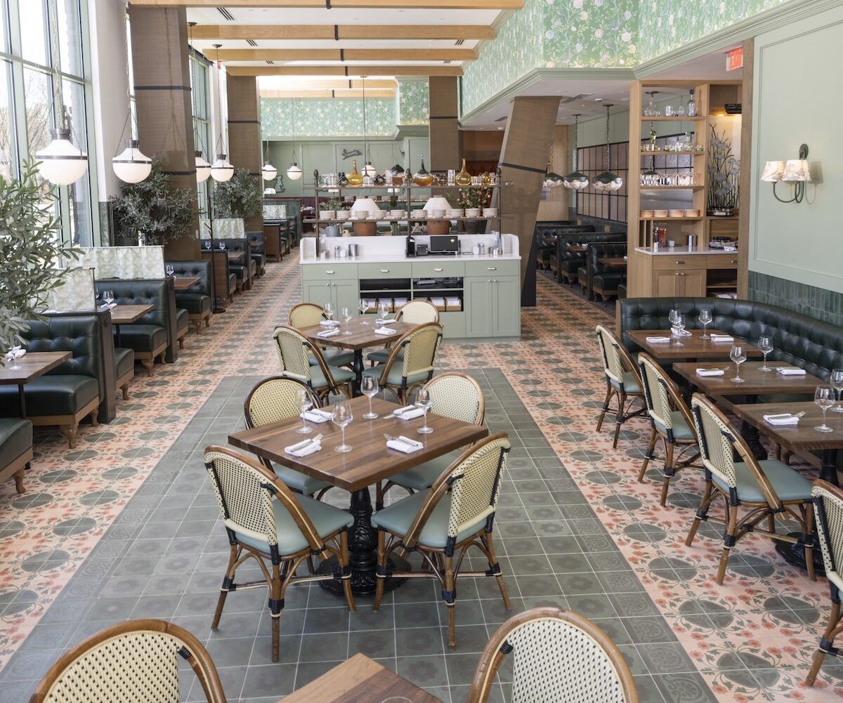 Bright and spacious dining room at Founding Farmers Alexandria featuring floral tile floors, green leather booths, wood tables, rattan chairs, and large windows offering natural light.
