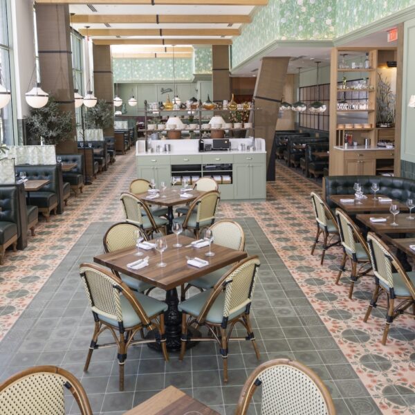 Bright and spacious dining room at Founding Farmers Alexandria featuring floral tile floors, green leather booths, wood tables, rattan chairs, and large windows offering natural light.