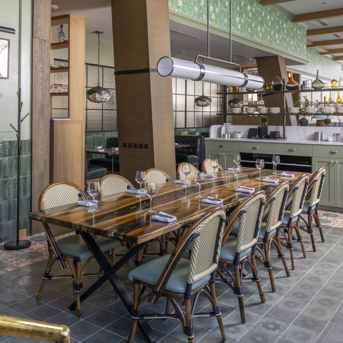 Intimate private dining area at Founding Farmers Alexandria featuring a polished wood table, rattan bistro chairs, floral green tile floors, and pendant lighting.