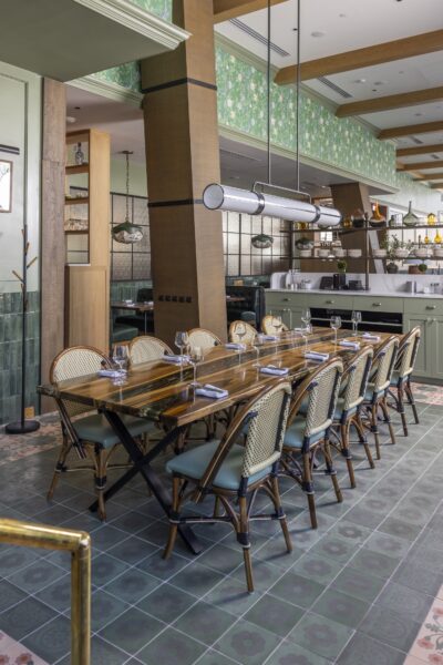 Intimate private dining area at Founding Farmers Alexandria featuring a polished wood table, rattan bistro chairs, floral green tile floors, and pendant lighting.